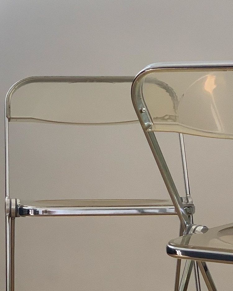 Two folding chairs in clear acrylic against a pale wall.