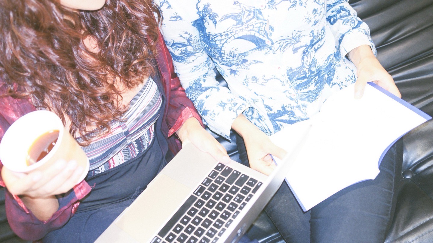 The two of us from above on the studio sofa, a laptop open across one lap, a coffee in one hand and an open notebook in the other.